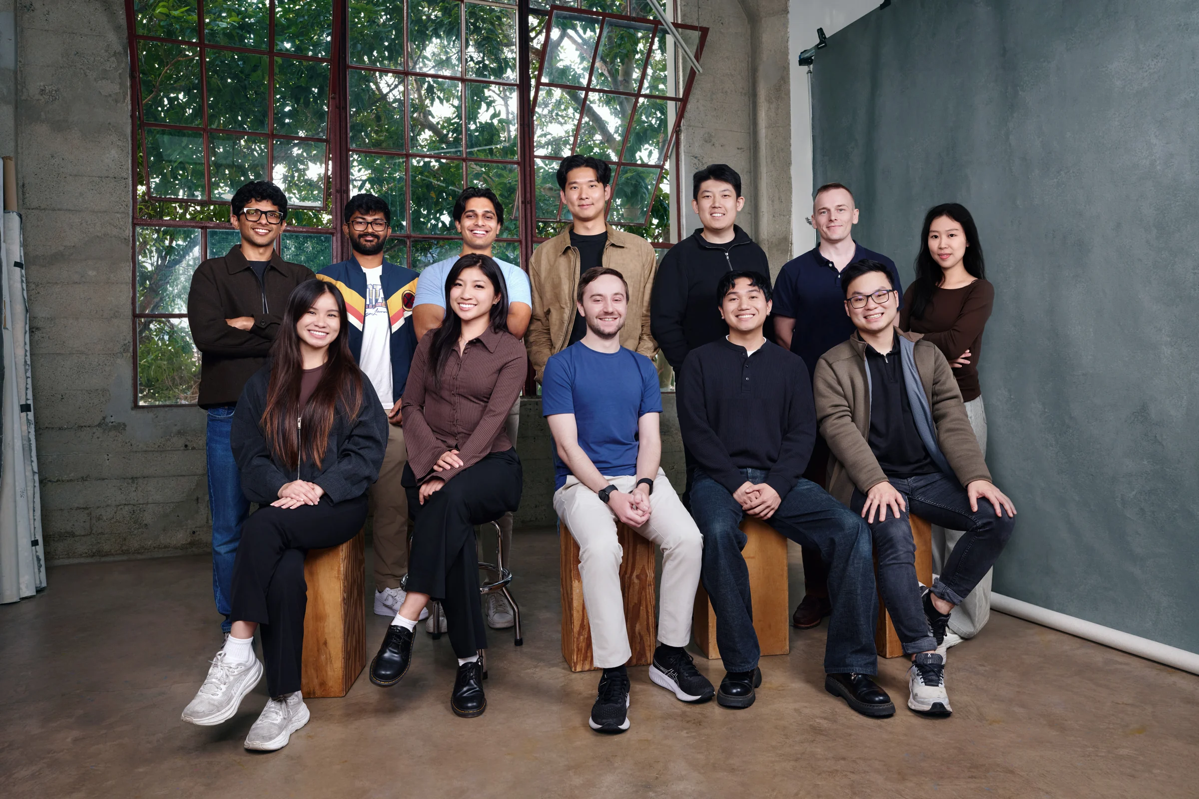 The Dream Labs team, twelve people, standing and sitting on wooden blocks in a studio with tall factory windows